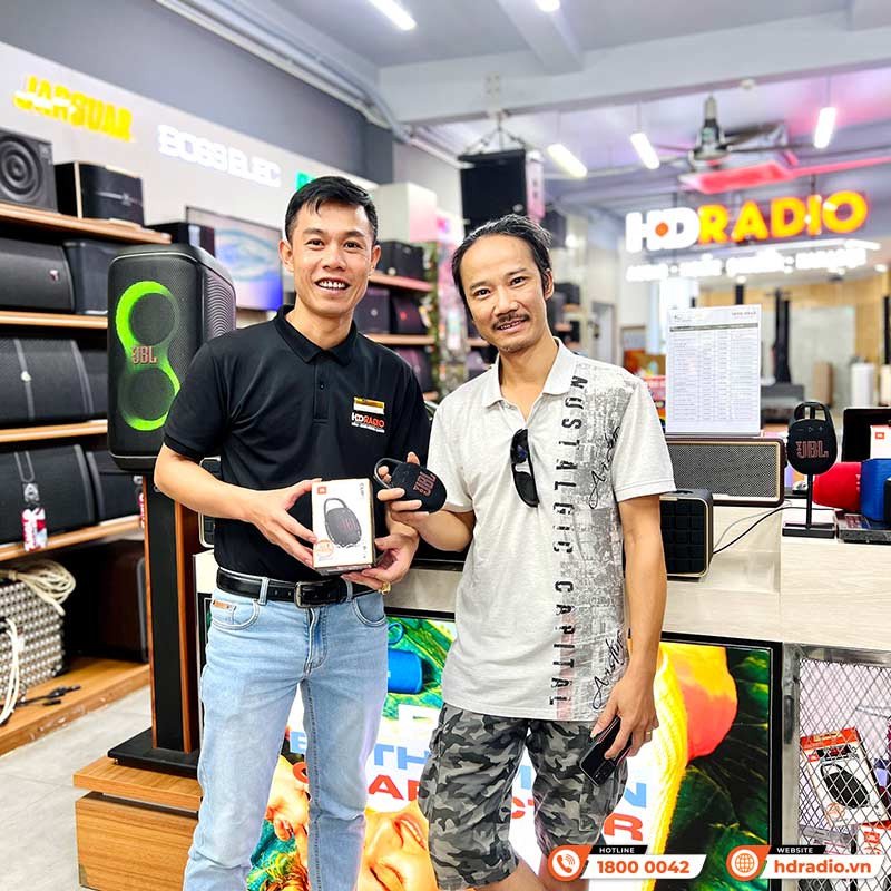 Một người phụ nữ trẻ đang tận hưởng âm nhạc từ loa JBL Clip 5 màu hồng được gắn vào túi xách của mình