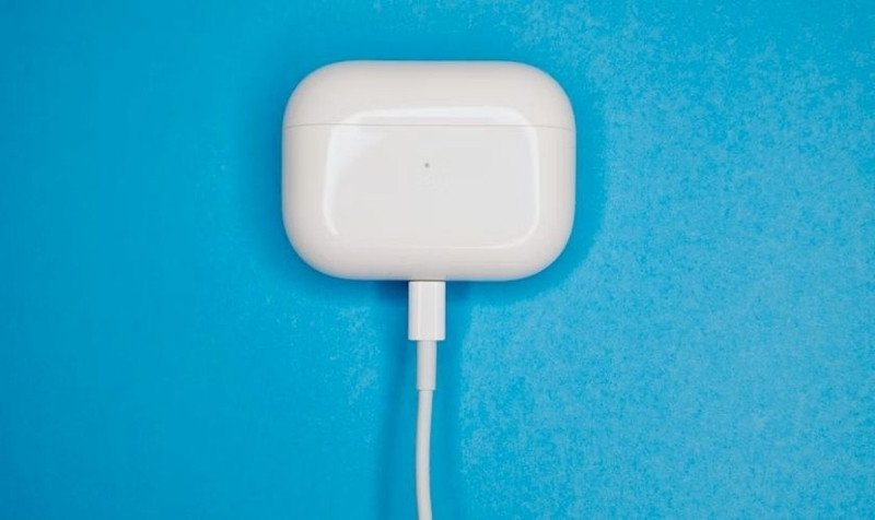 Hộp sạc tai nghe không dây màu trắng đang được cắm sạc bằng cáp USB-C, đặt trên bề mặt sạch sẽ.