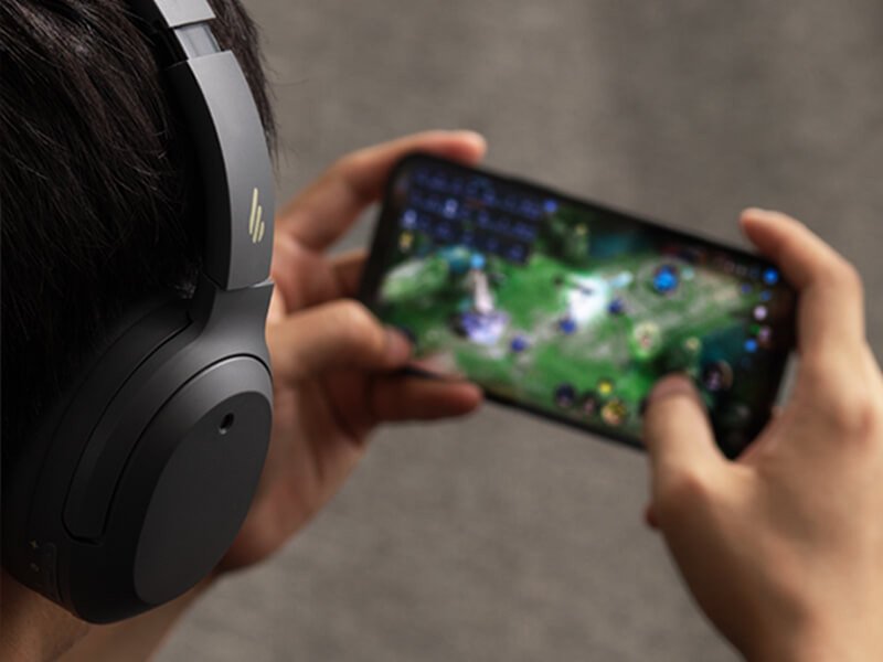 Người dùng đeo tai nghe chơi game Edifier W820NB tập trung vào màn hình, minh họa chế độ chơi game độ trễ thấp.